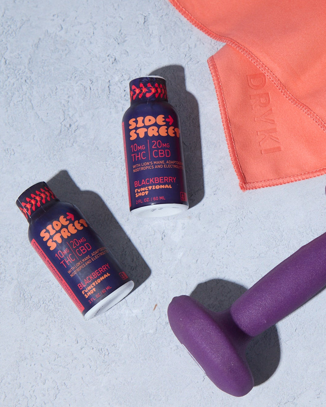 Two bottles of Side Street Sport, a purple dumbbell, and an orange towel on a light gray surface.