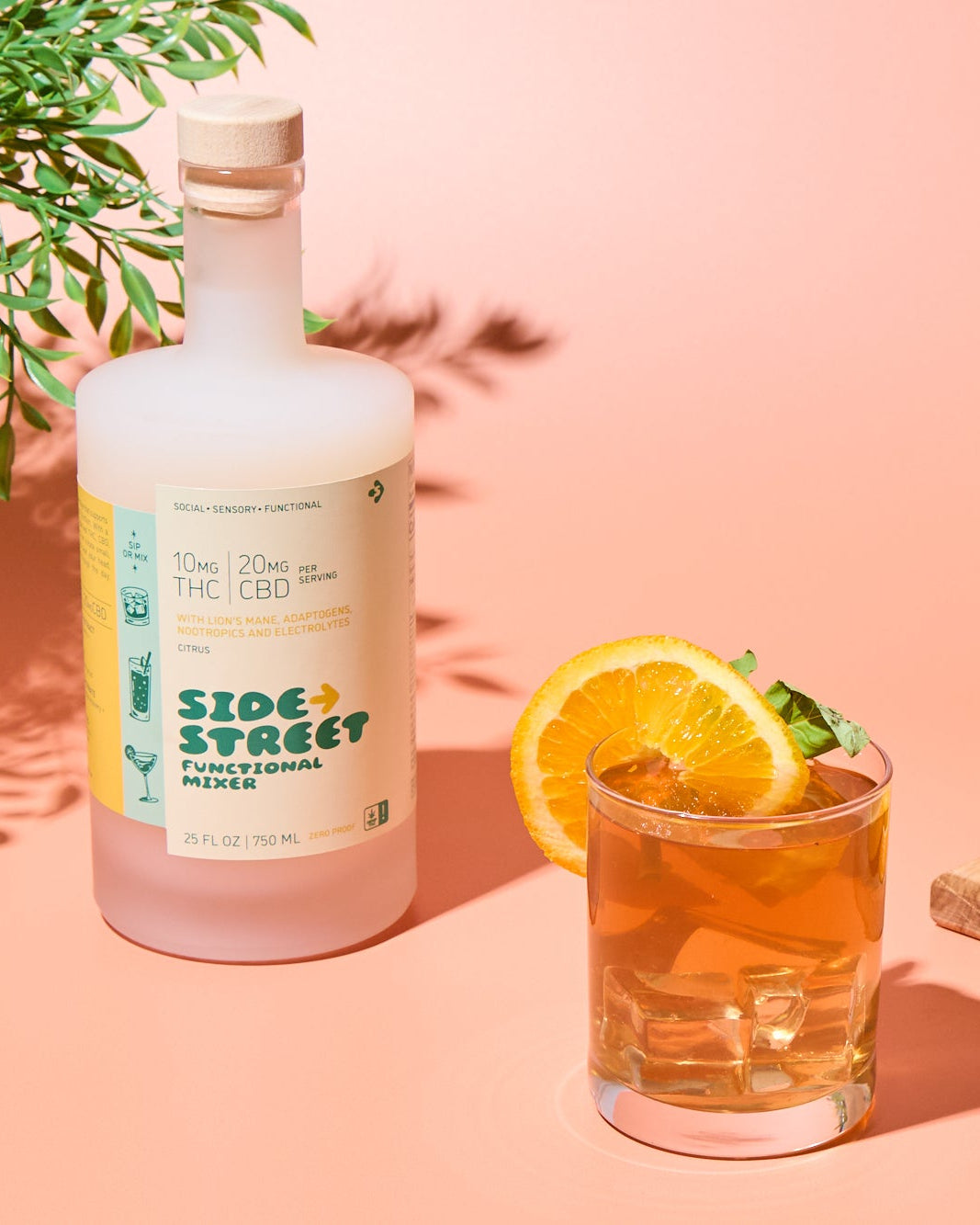 Bottle of Sidestreet with a cocktail and oranges on a pink background
